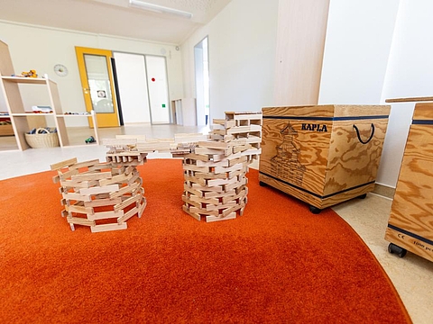 Ein Raum mit einem großen runden Teppich; in der Mitte steht ein von Kindern gebautes, rundes Holzwerk aus dicken Holzstäben, das in die Höhe ragt