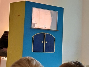 aufgestelltes, buntes Puppentheater, das beleuchtet wird und auf dem Schattenfiguren zu sehen sind