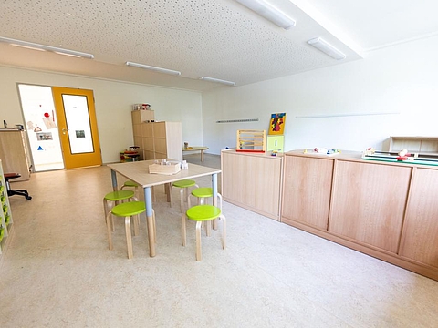 Ein Spielraum mit Holztischen und Holzregalen, auf denen verschiedene Spielzeuge ordentlich bereitgestellt sind