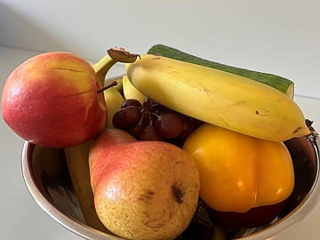 Eine Metallschüssel mit Apfel, Birne, Banane, Weintrauben, Gurke und gelber Paprika