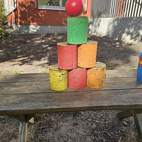 In einer Pyramide aufgestellte bunte Dosen mit einem roten Ball auf der Spitze