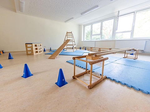 Ein Bewegungsraum mit blauen Matten, verschiedenen Klettermöglichkeiten und blauen Hütchen