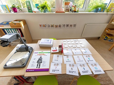 Ein Tisch mit einem Projektor und Lernblättern, die Kindern helfen, Zahlen zu erkennen und zu verstehen.