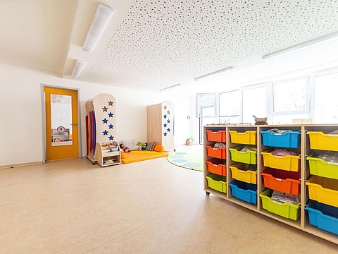Ein großer Schlafraum mit viel Platz; auf der rechten Seite ist ein Regal zur Aufbewahrung der Schlafsachen der Kinder. Im Hintergrund liegen Kuscheltiere und Kissen.